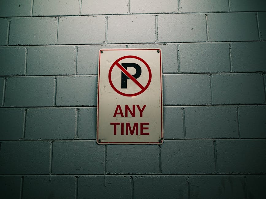 A metal garage door painted in horizontal grey slats displays three signs in a row. The two outer signs are white with a red circle and a diagonal slash over a black 'P', indicating no parking. The ce